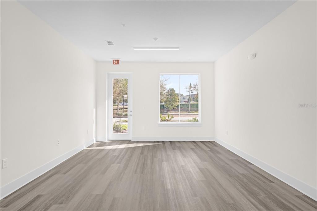 An empty room features light wood-look flooring, white walls, a glass door, and a window — 415 MIKE ROBERTO WAY, OVIEDO, FL