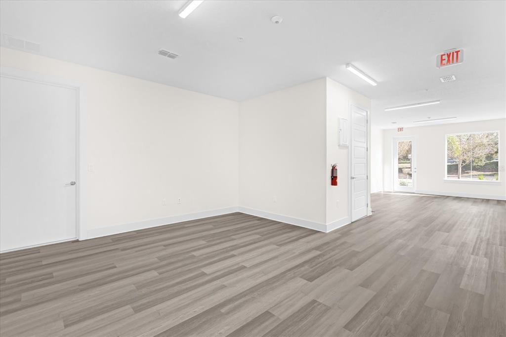 An empty commercial space features light wood-look flooring, white walls, and multiple exit signs — 415 MIKE ROBERTO WAY, OVIEDO, FL