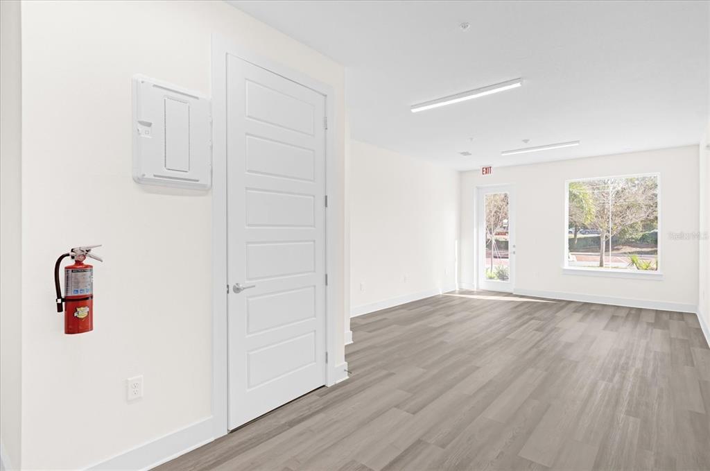 An empty room with light wood-look flooring, a white door, and a wall-mounted fire extinguisher — 415 MIKE ROBERTO WAY, OVIEDO, FL
