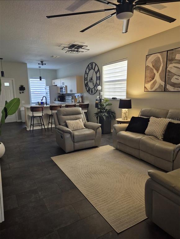 An open-concept living room features gray leather furniture, a large wall clock, and kitchen seating — 6102 LAKE MARION GOLF RESORT, KISSIMMEE, FL