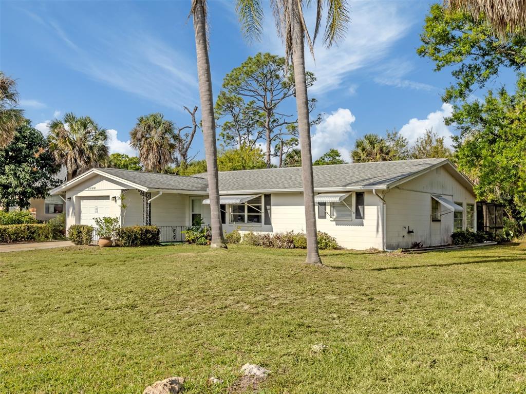 A single-story house with a white exterior, metal awnings, and palm trees in the yard — 3180 FALLOW ROAD, VENICE, FL