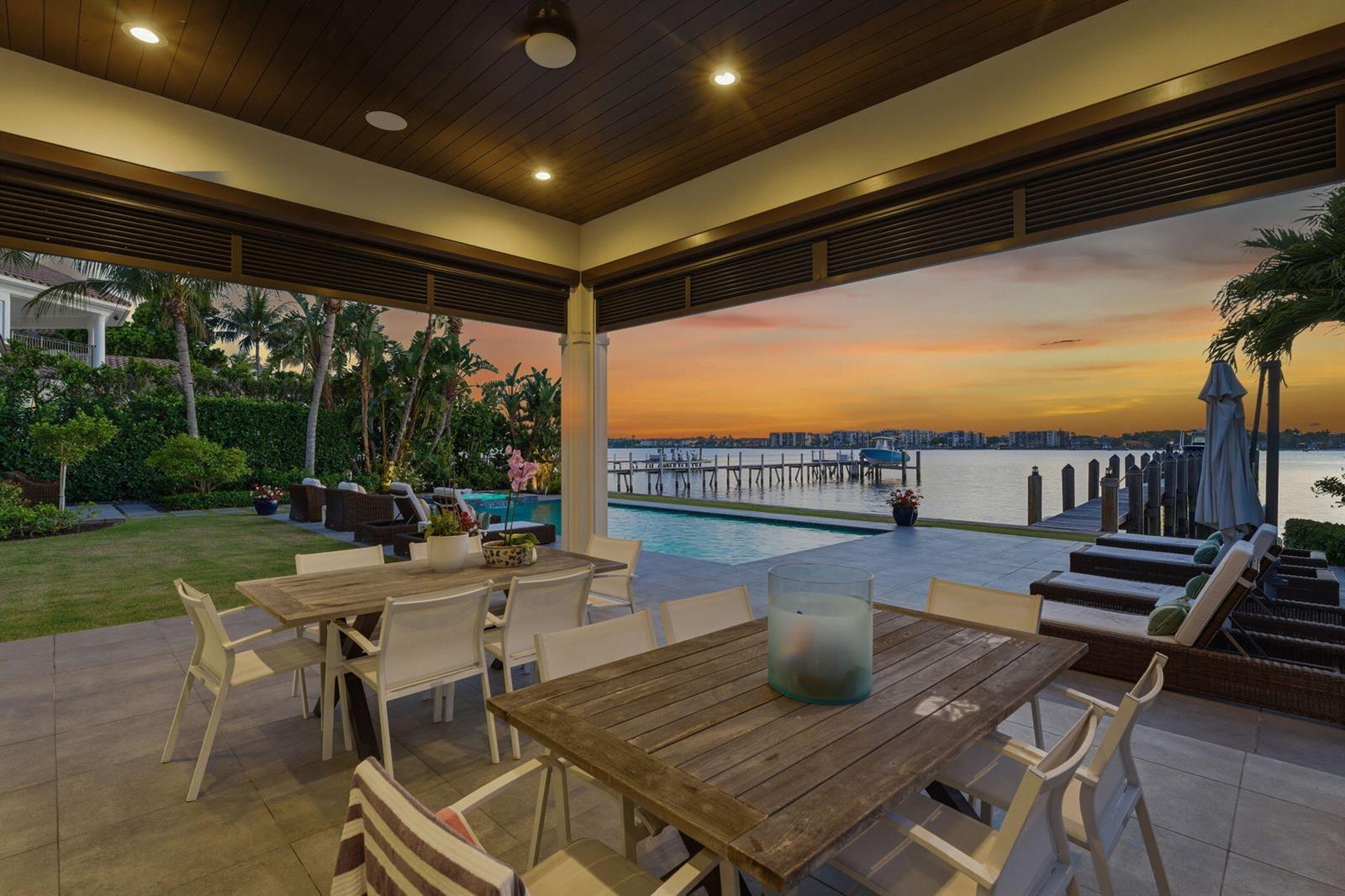 A covered patio features two dining tables, lounge chairs, and a pool overlooking the water — 825 W Oyster Lane, Lantana FL 33462, LANTANA, FL