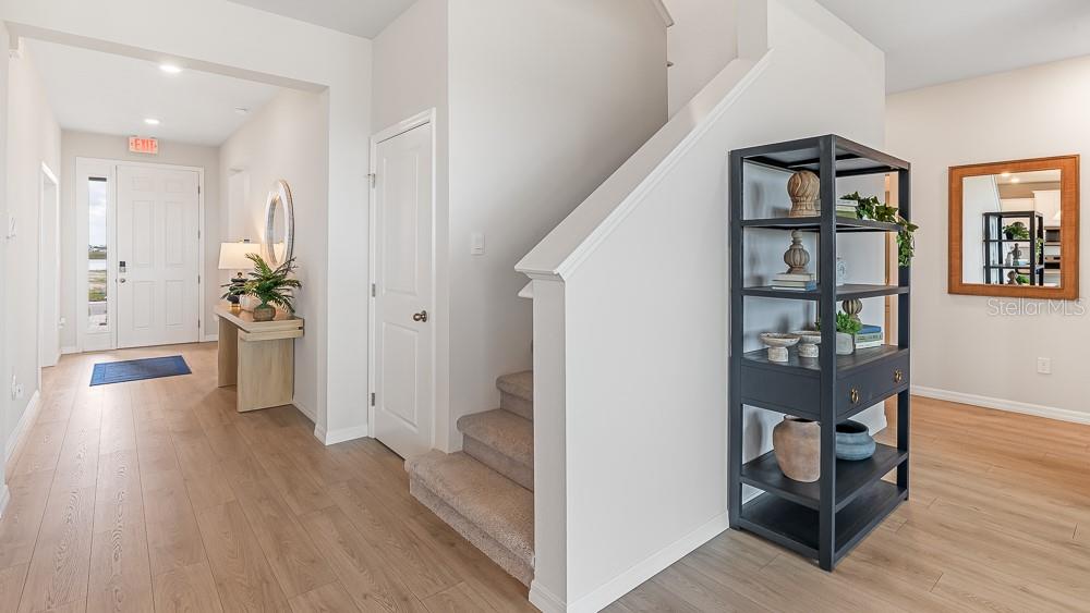 A bright entryway features light wood flooring, a staircase with carpeted steps, and a dark bookshelf — 10742 RABBIT GROVE TRAIL, PARRISH, FL