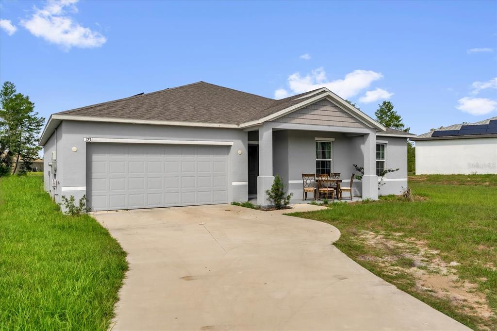A single-story house with a gray stucco exterior, a two-car garage, and a covered porch — 123 ZINNIA LANE W, POINCIANA, FL