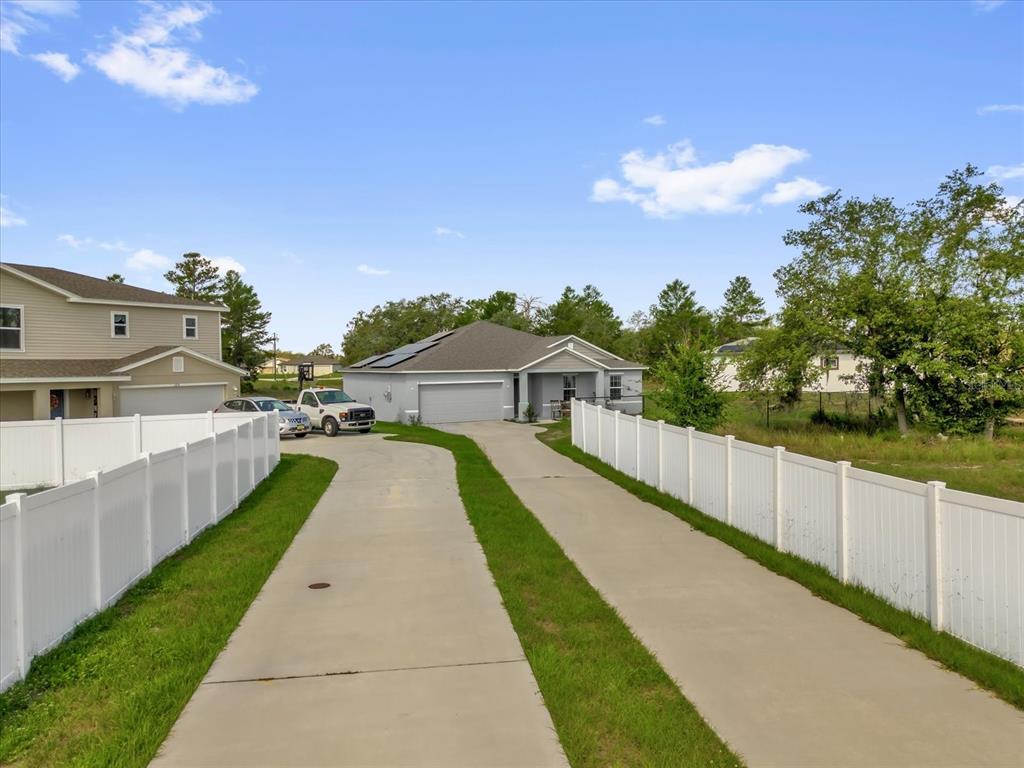 A concrete driveway leads to a single-story house with solar panels and white vinyl fencing — 123 ZINNIA LANE W, POINCIANA, FL