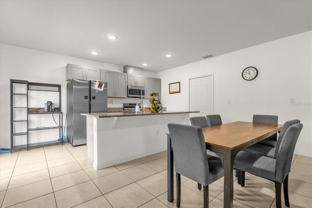 A kitchen with grey cabinets and stainless steel appliances opens to a dining area — 123 ZINNIA LANE W, POINCIANA, FL