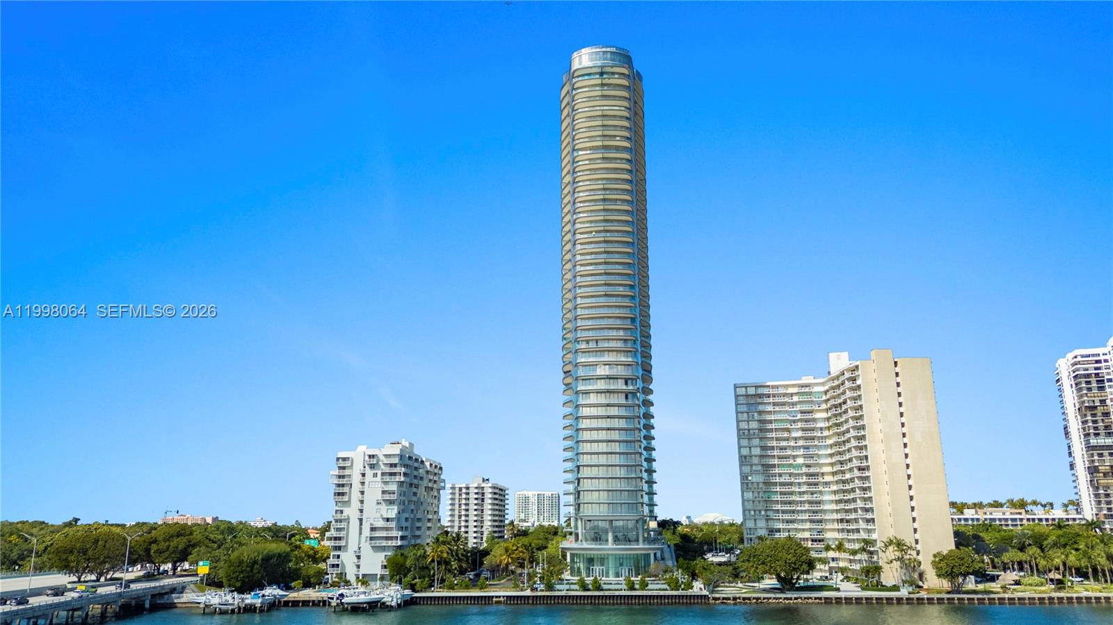 A tall, cylindrical residential skyscraper stands prominently against a clear blue sky near water — 175 SE 25 Rd # 2003, Miami FL 33129, MIAMI, FL