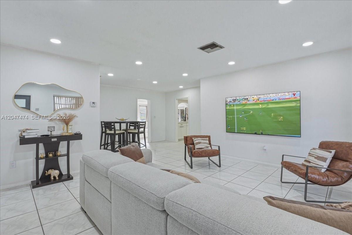 A living room features white tile floors, a gray sectional sofa, and a wall-mounted television — 7850 W 16th Ave, Hialeah FL 33014, HIALEAH, FL