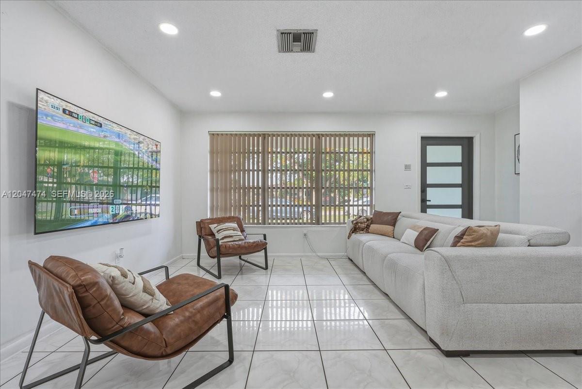 A living room features white tiled floors, a large wall-mounted television, and modern furniture — 7850 W 16th Ave, Hialeah FL 33014, HIALEAH, FL