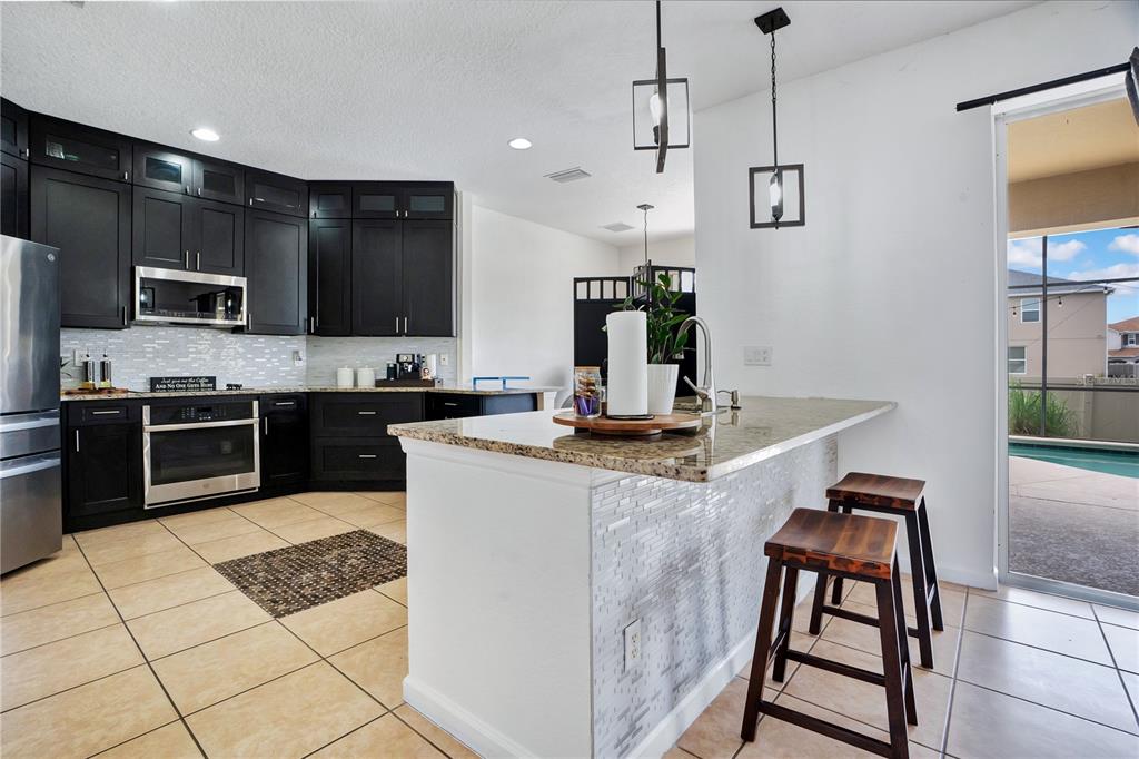 A kitchen features dark cabinets, granite countertops, a breakfast bar with stools, and tile flooring — 3571 MAPLE RIDGE LOOP, KISSIMMEE, FL