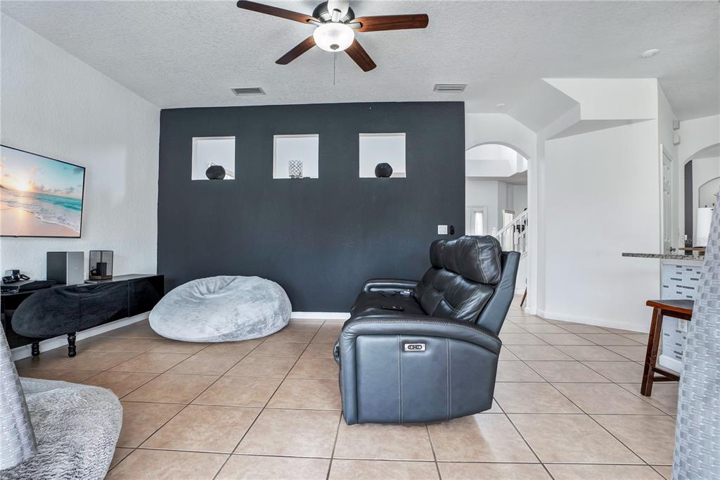 A living room features a dark accent wall with three niches, tile flooring, and a recliner — 3571 MAPLE RIDGE LOOP, KISSIMMEE, FL