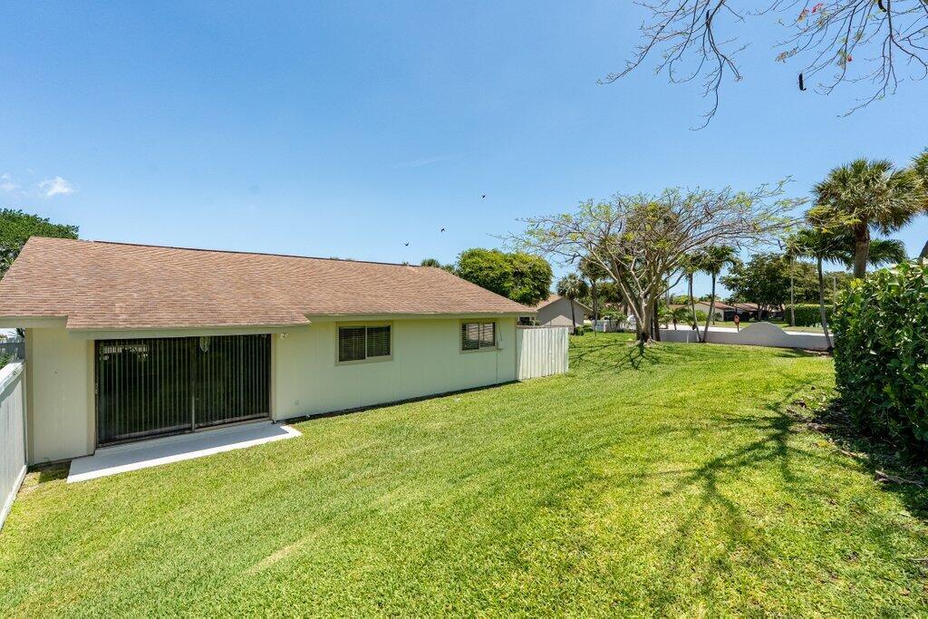A view of a house exterior with a grassy yard, sliding glass doors, and trees — 1 Afton Place, Boynton Beach FL 33426, BOYNTON BEACH, FL