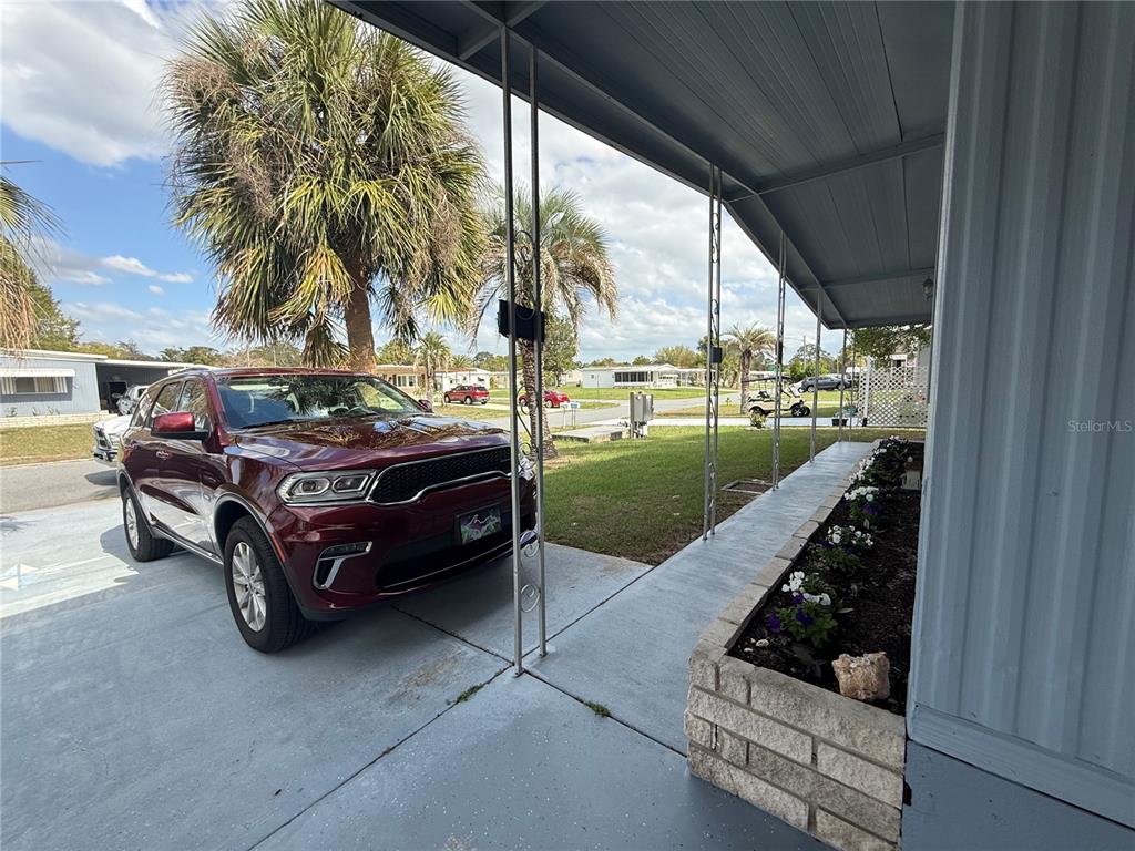 A maroon SUV is parked under a covered carport next to a brick planter box — 7441 FAIRLANE AVENUE, BROOKSVILLE, FL