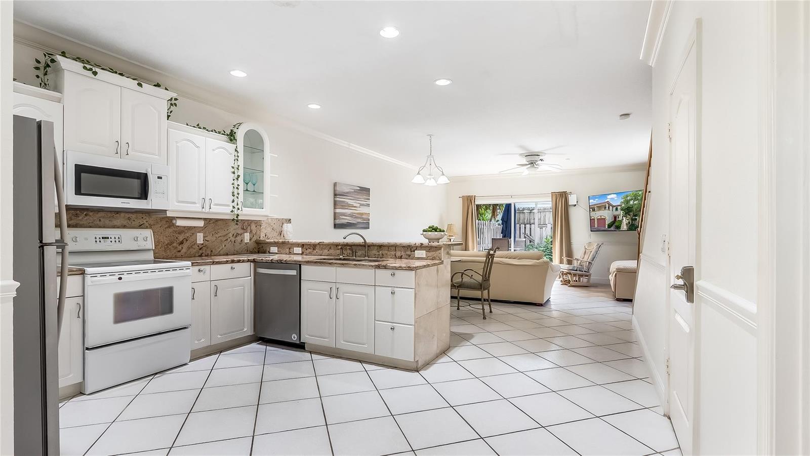 A kitchen with white cabinets and granite countertops opens into a living area with tile — 512 S Ocean Boulevard, Pompano Beach FL 33062, POMPANO BEACH, FL