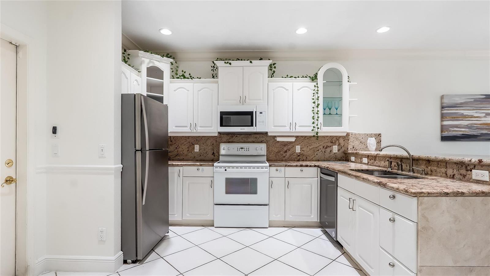 A kitchen features white cabinets, a stainless steel refrigerator, a white stove, and granite countertops — 512 S Ocean Boulevard, Pompano Beach FL 33062, POMPANO BEACH, FL