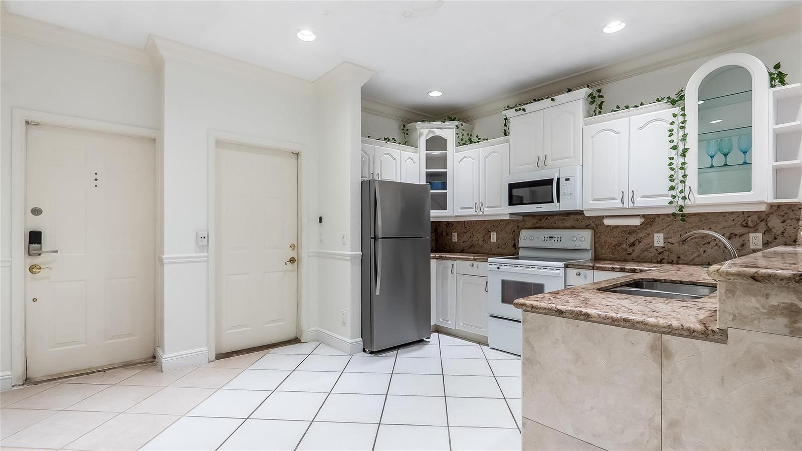 A kitchen features white cabinets, stainless steel appliances, granite countertops, and white tile flooring — 512 S Ocean Boulevard, Pompano Beach FL 33062, POMPANO BEACH, FL