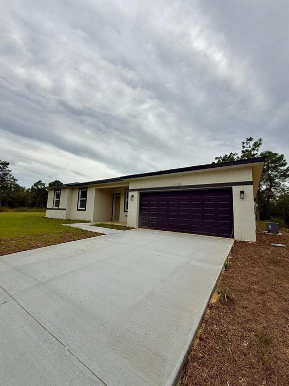 A single-story house with a beige stucco exterior, a dark garage door, and a concrete driveway — 11128 N G MARTINELLI BOULEVARD, CITRUS SPRINGS, FL