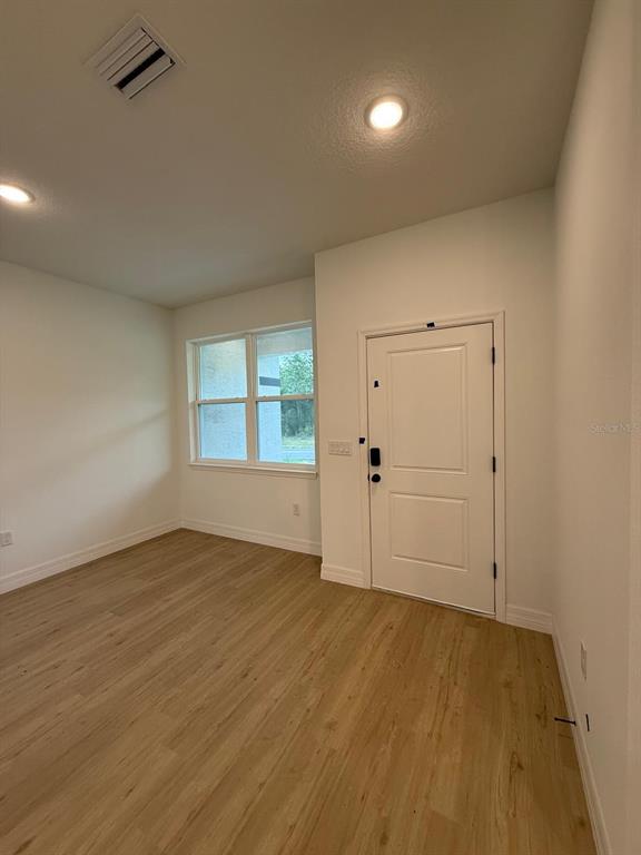 An empty room with light wood-look flooring, a window, and a white entry door — 11128 N G MARTINELLI BOULEVARD, CITRUS SPRINGS, FL