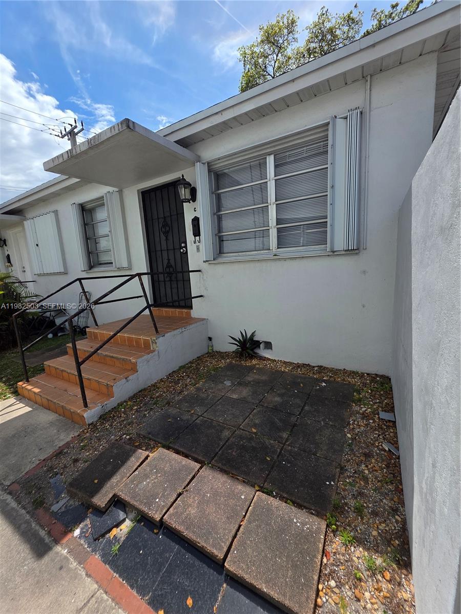 A white exterior building features a small concrete patio, tiled steps, and a metal security door — 57 Esplanade Dr # C, Miami Springs FL 33166, MIAMI SPRINGS, FL