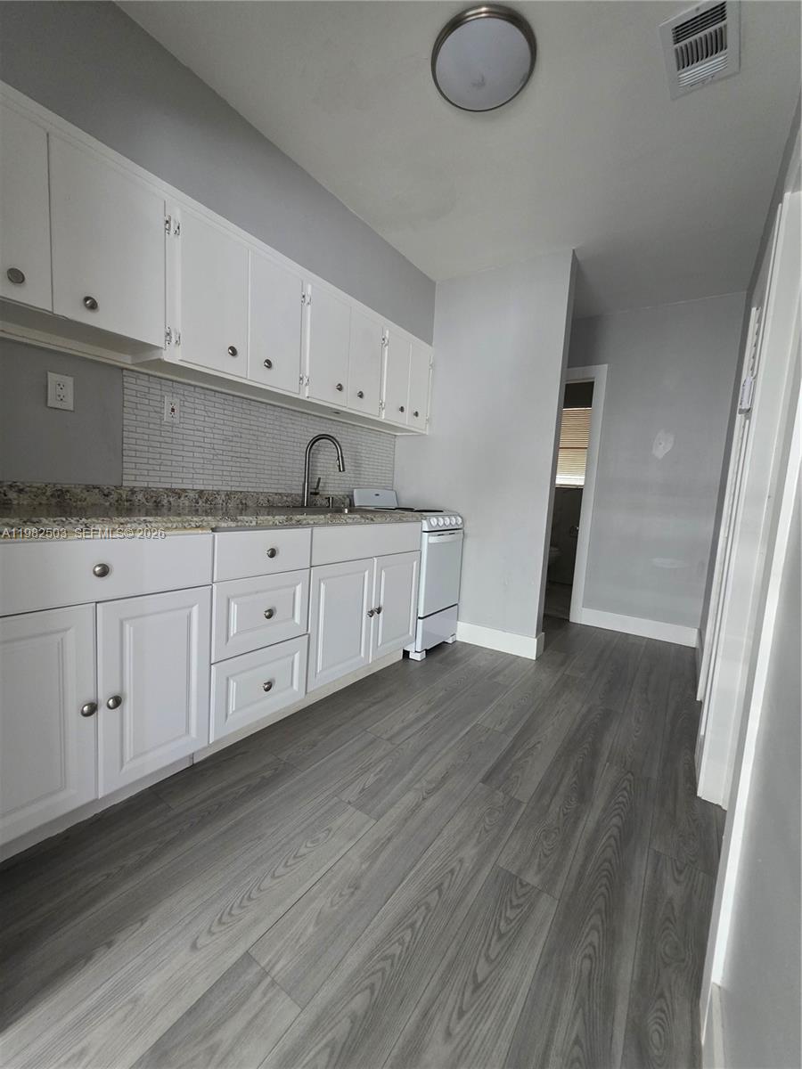 A kitchen features white cabinets, granite countertops, a tiled backsplash, and gray wood-look flooring — 57 Esplanade Dr # C, Miami Springs FL 33166, MIAMI SPRINGS, FL