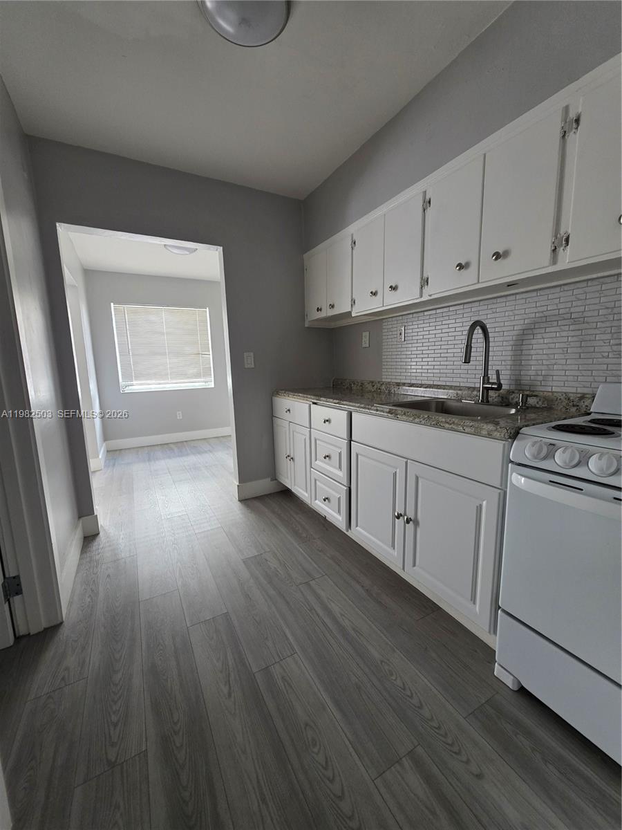 A kitchen features white cabinets, a granite countertop, a tiled backsplash, and light wood flooring — 57 Esplanade Dr # C, Miami Springs FL 33166, MIAMI SPRINGS, FL