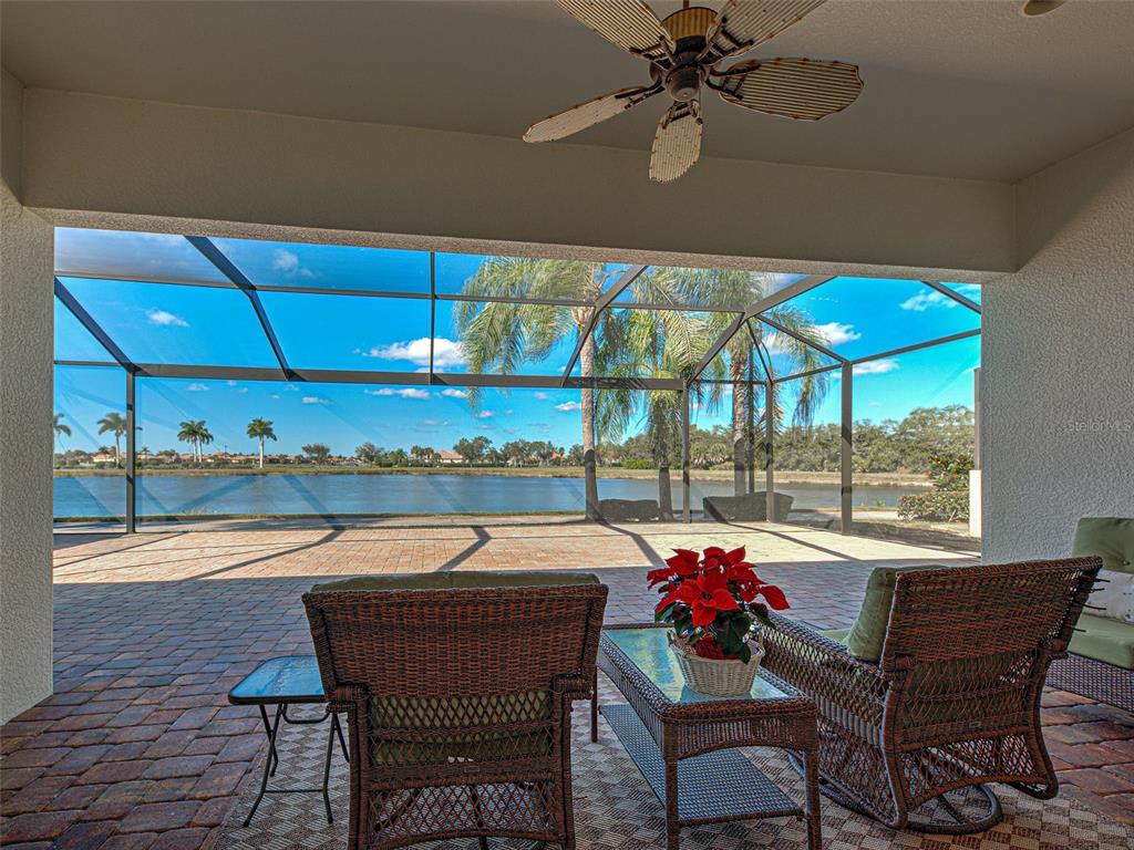 A covered patio with wicker furniture overlooks a screened-in pool deck and a lake — 19267 KIRELLA STREET, VENICE, FL