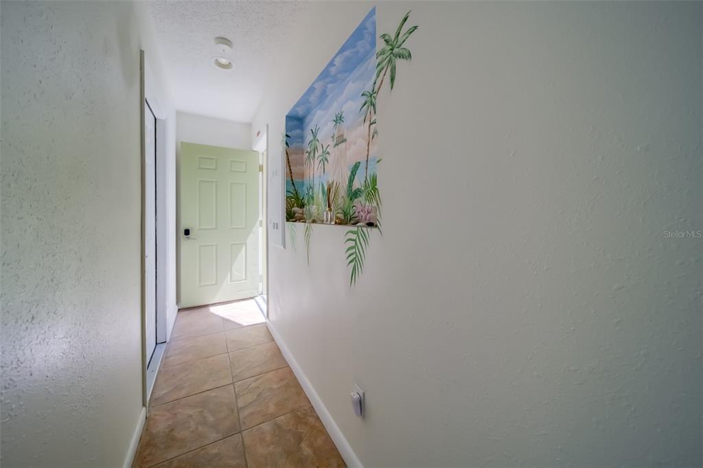 A hallway with tiled flooring leads to a light green door featuring a wall mural — 18111 1ST STREET E, REDINGTON SHORES, FL