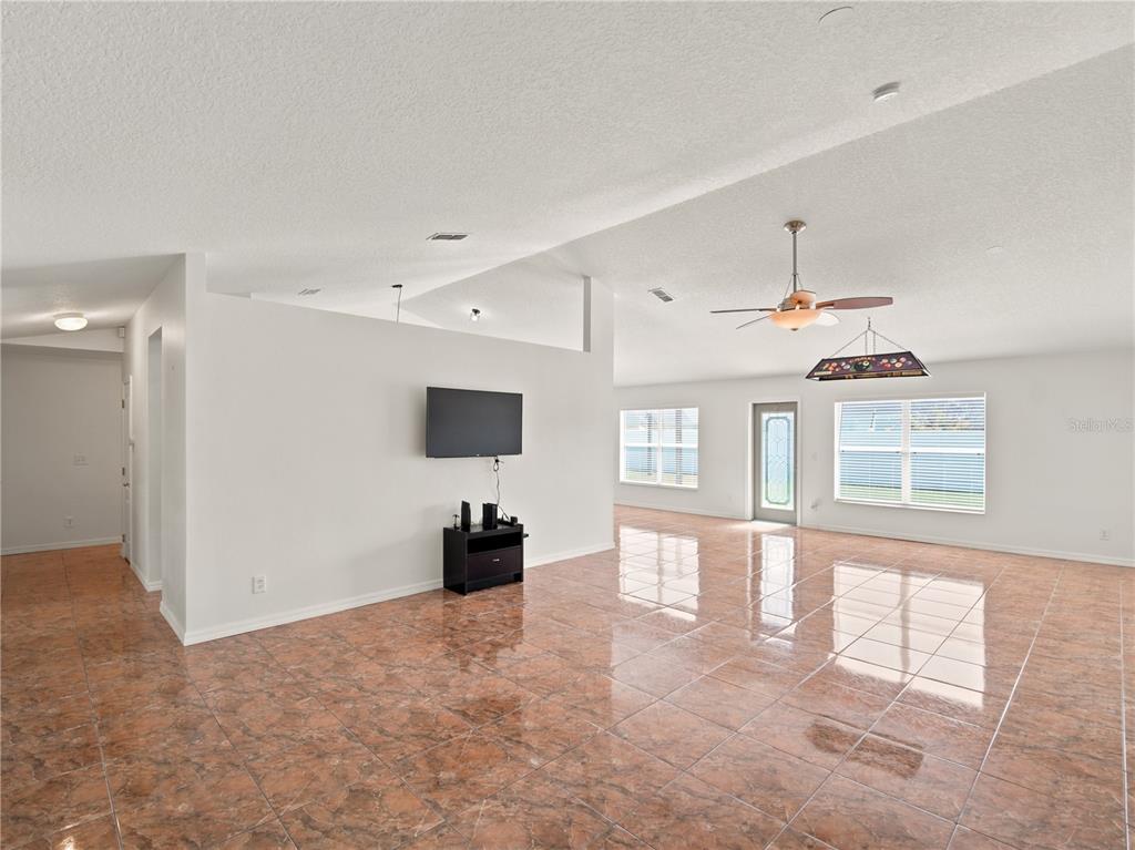 A spacious living area features glossy brown tile flooring, a vaulted ceiling, and a wall-mounted television — 6013 BRICK ROAD, ST CLOUD, FL