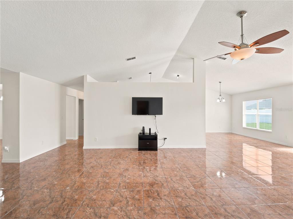 A living room with vaulted ceilings, tile flooring, a wall-mounted television, and a ceiling fan — 6013 BRICK ROAD, ST CLOUD, FL