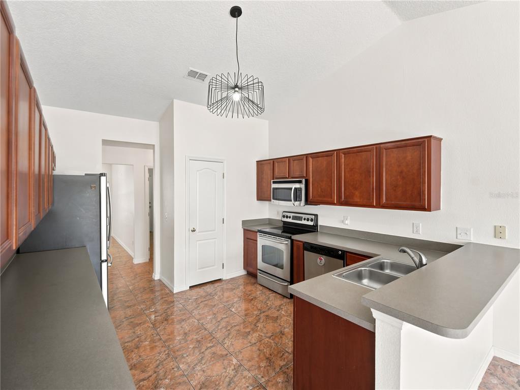 A kitchen features brown cabinets, stainless steel appliances, gray countertops, and brown tile flooring — 6013 BRICK ROAD, ST CLOUD, FL