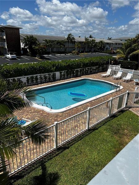 An elevated view of a rectangular swimming pool surrounded by a white fence and patio — 701 Pine Drive # 204, Pompano Beach FL 33060, POMPANO BEACH, FL