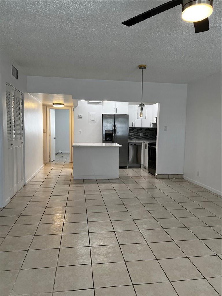 A tiled living area opens to a kitchen with stainless steel appliances and a white island — 701 Pine Drive # 204, Pompano Beach FL 33060, POMPANO BEACH, FL