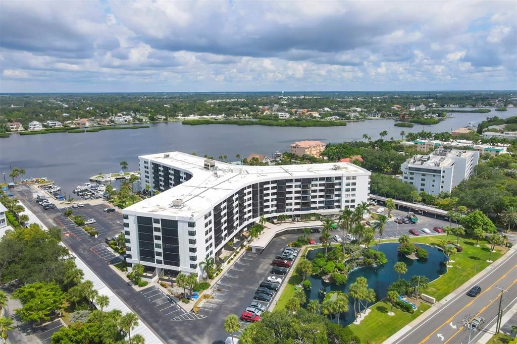An aerial view shows a large multi-story apartment complex with a parking lot and pond — 5855 MIDNIGHT PASS ROAD UNIT 420, SARASOTA, FL