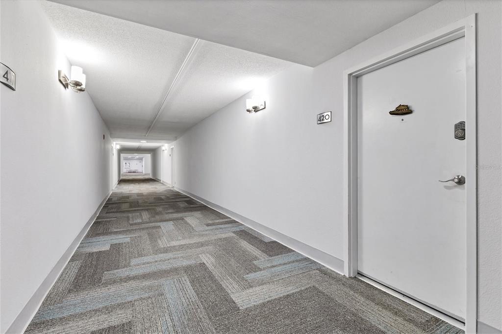 A long, white-walled apartment hallway features patterned gray carpet and a door labeled 420 — 5855 MIDNIGHT PASS ROAD UNIT 420, SARASOTA, FL