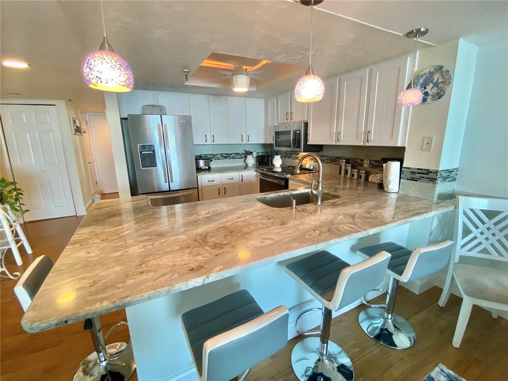A kitchen features white cabinets, a large stone island, and three bar stools — 6035 SEA RANCH DRIVE UNIT 901, HUDSON, FL
