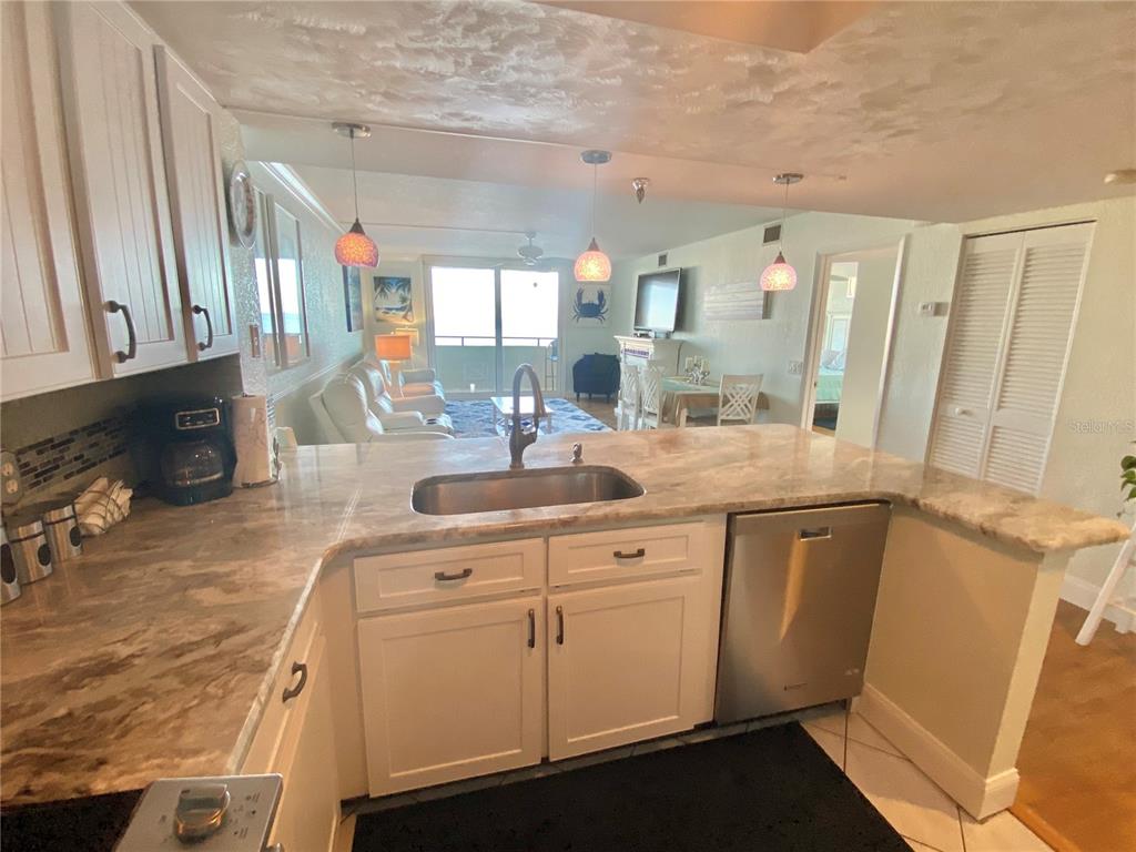 A kitchen with white cabinets and stone countertops overlooks a living area with ocean views — 6035 SEA RANCH DRIVE UNIT 901, HUDSON, FL