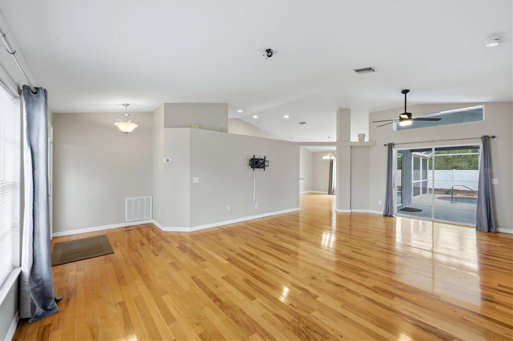 An open-concept living area features hardwood floors, vaulted ceilings, and sliding glass doors to a pool — 3575 LUBEC AVENUE, NORTH PORT, FL