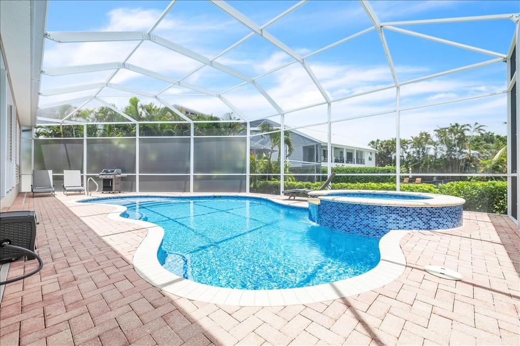 A swimming pool and attached hot tub sit on a brick patio inside a screened enclosure — 6050 TIDEWATER ISLAND CIRCLE, FORT MYERS, FL