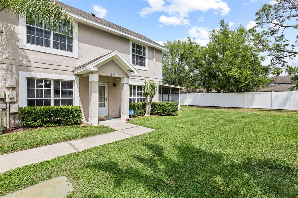 A two-story beige townhouse exterior with a front walkway, small porch, and white privacy fence — 539 KENSINGTON LAKE CIRCLE, BRANDON, FL