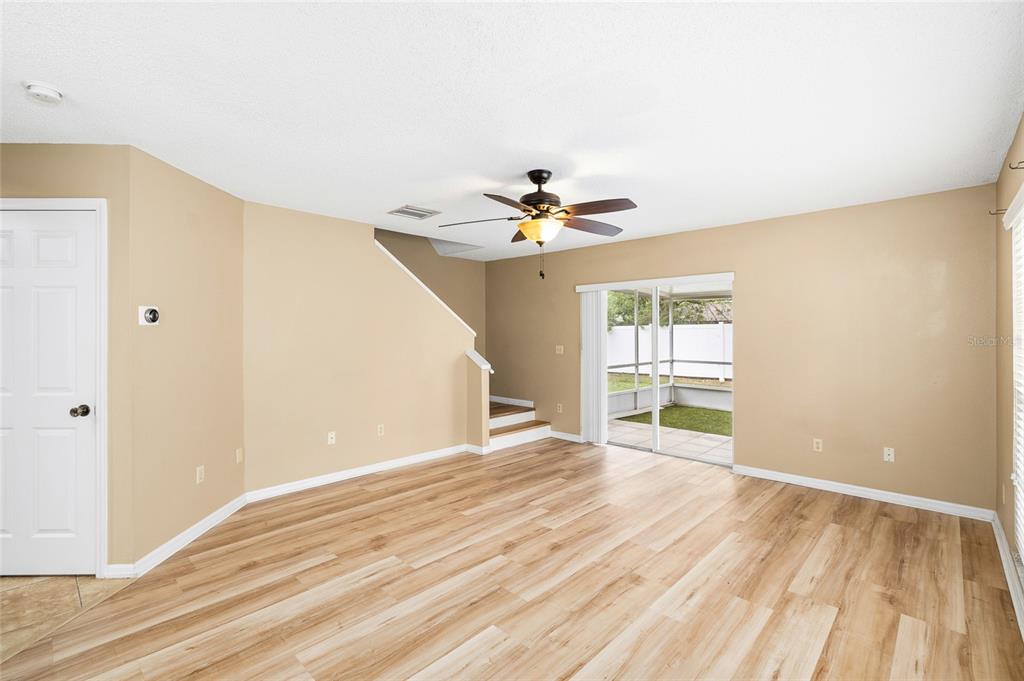 A living room with light wood-look flooring, a ceiling fan, and a sliding glass door — 539 KENSINGTON LAKE CIRCLE, BRANDON, FL