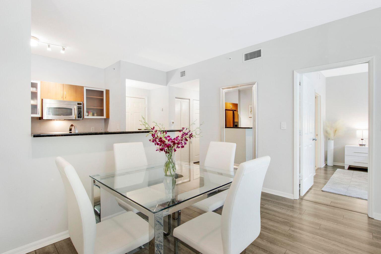 A dining area with a glass table, four white chairs, and an adjacent open kitchen — 802 W Windward Way # 206, Lantana FL 33462, LANTANA, FL