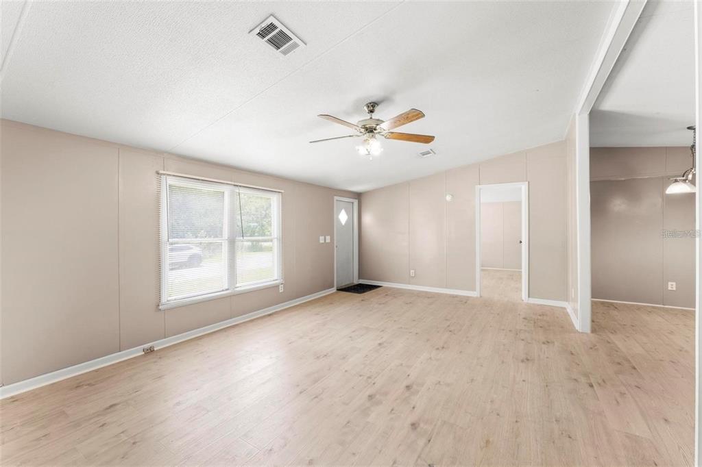 A spacious living room features light-colored wood-look flooring, beige walls, a ceiling fan, and windows — 201 N 5TH STREET, ORLANDO, FL