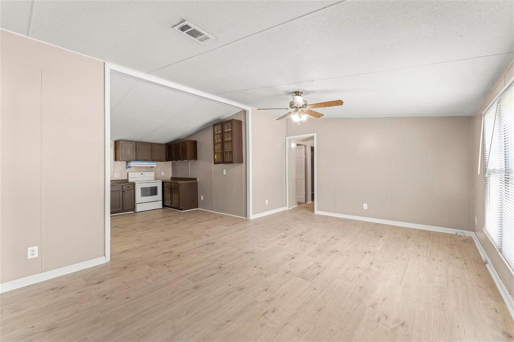 An open-concept living room with light wood-look flooring leads into a kitchen with dark cabinets — 201 N 5TH STREET, ORLANDO, FL