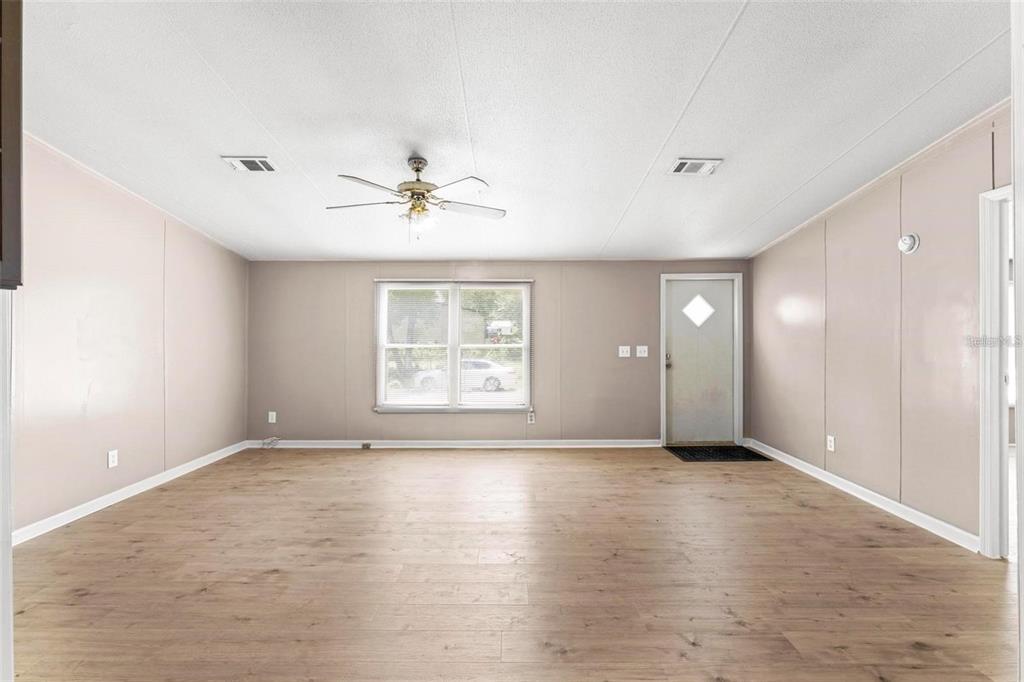 An empty living room features light-colored wood-look flooring, beige walls, a ceiling fan, and windows — 201 N 5TH STREET, ORLANDO, FL
