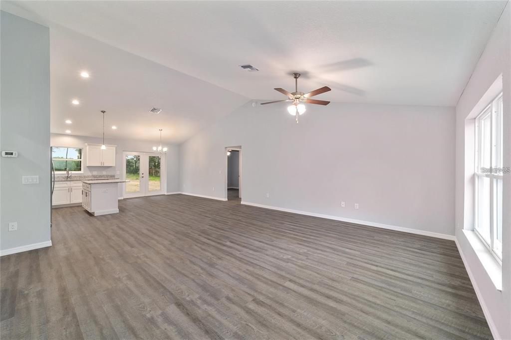 An open-concept living room and kitchen with vaulted ceilings, gray flooring, and white cabinetry — 6459 SW 204TH AVENUE, DUNNELLON, FL