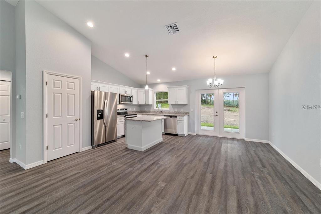 A kitchen with white cabinets, stainless steel appliances, and an island opens to a dining area — 6459 SW 204TH AVENUE, DUNNELLON, FL