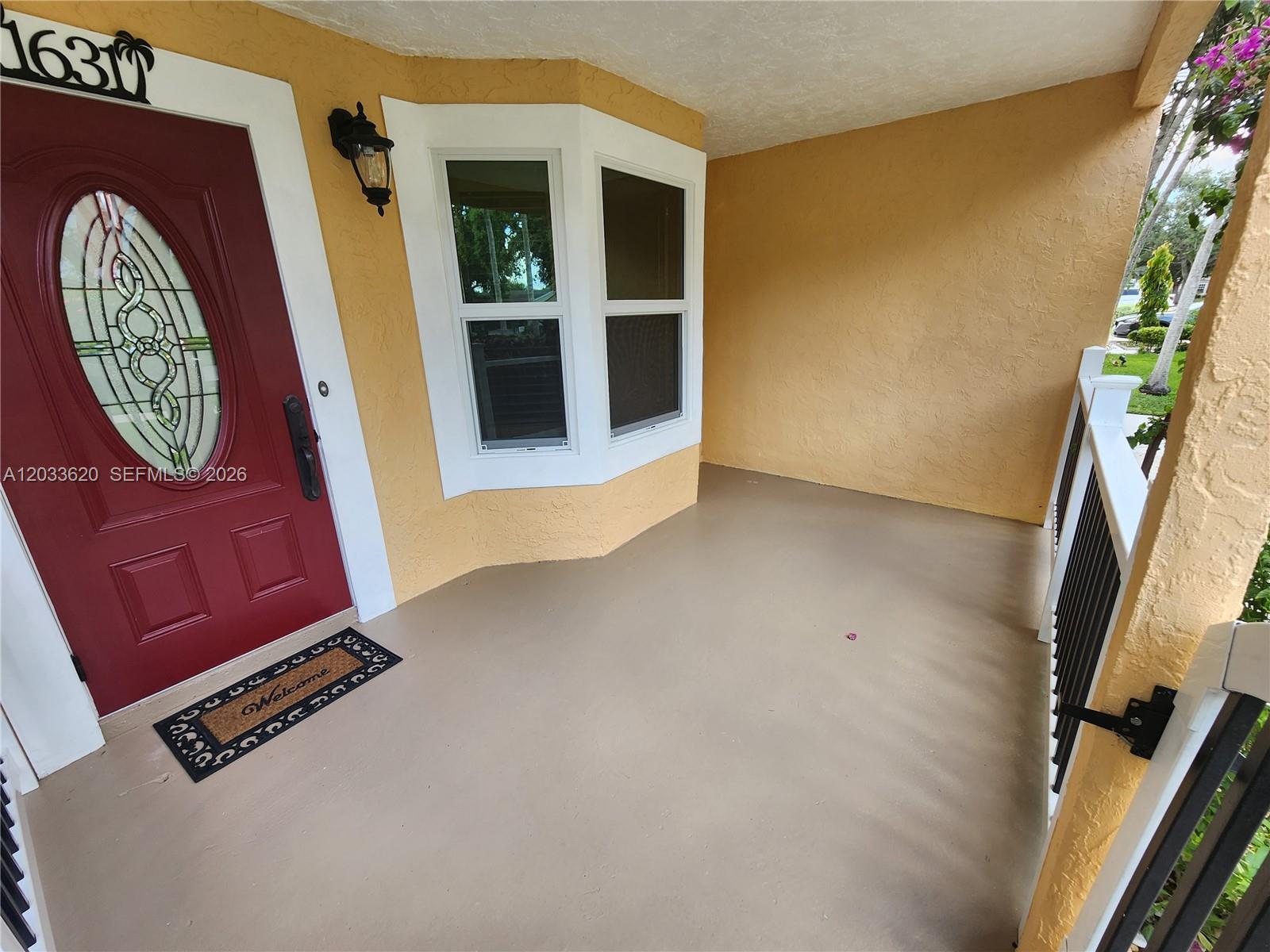 A covered front porch features a red door, a bay window, and tan walls — DAVIE, FL