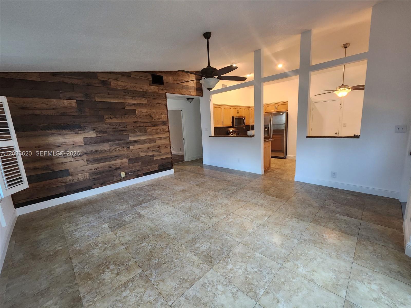 A living room features a wood-paneled accent wall, tile flooring, and an open kitchen view — DAVIE, FL