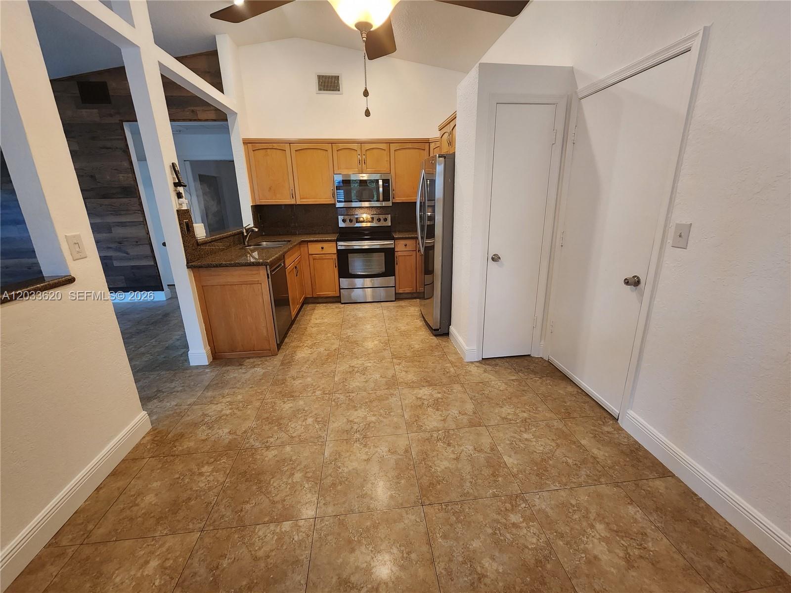 A kitchen features light wood cabinets, stainless steel appliances, and brown tile flooring — DAVIE, FL