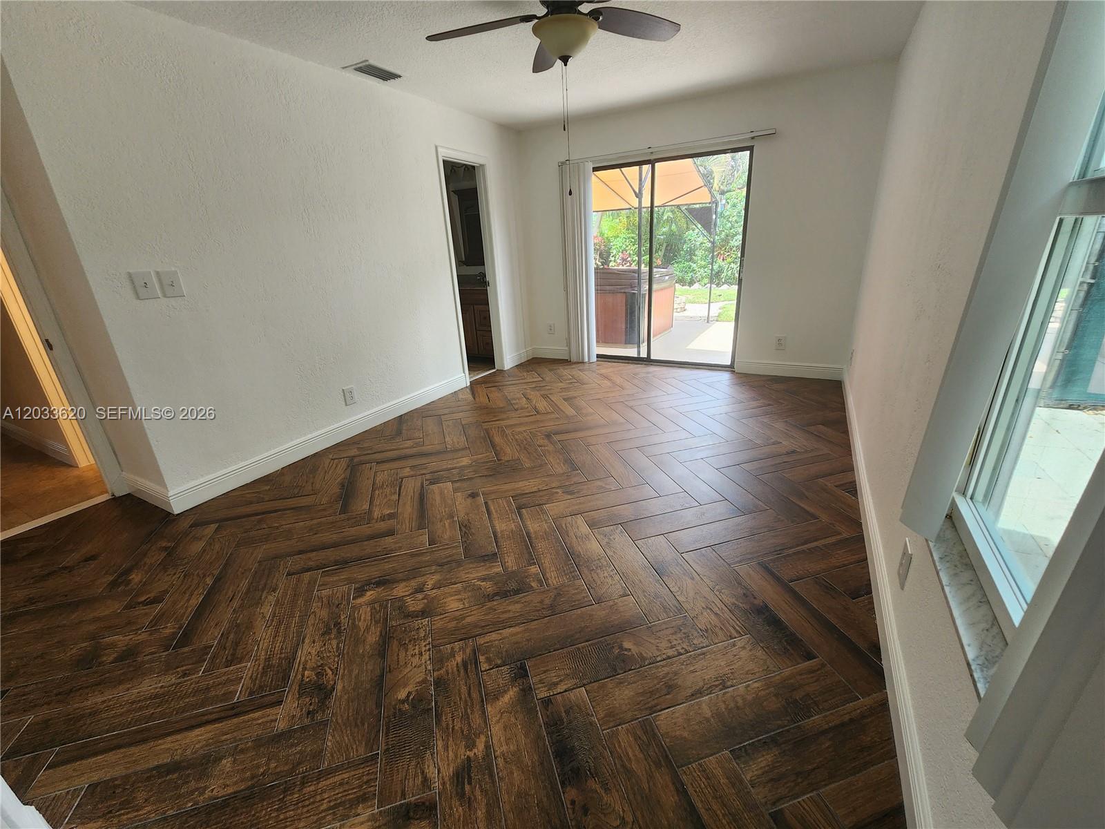 A room with herringbone-patterned wood-look flooring, a ceiling fan, and sliding glass doors — DAVIE, FL